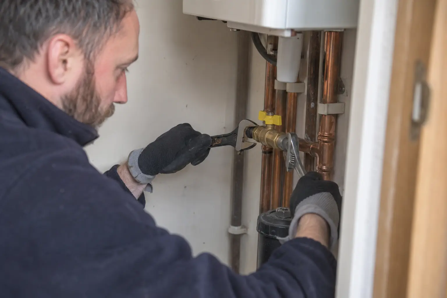 Gas valve replacement — Close documentary photo of a gas engineer replacing a small brass inline gas isolation valve on accessible copper pipework in a utility cupboard, two appropriate spanners supporting fittings, isolated supply, gloves, no sparks or flames.